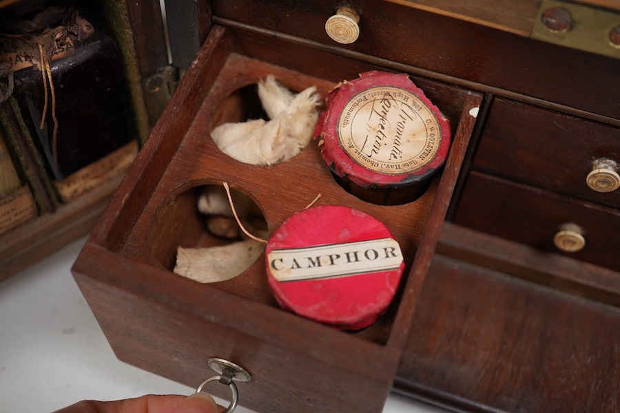 A 19th century mahogany apothecary cabinet, containing 20 bottles of various medicinal compounds and poisons, some sealed, all with paper labels, mainly for ‘C. Woollven, Operative & Dispensing Chemist, 108, High Street,